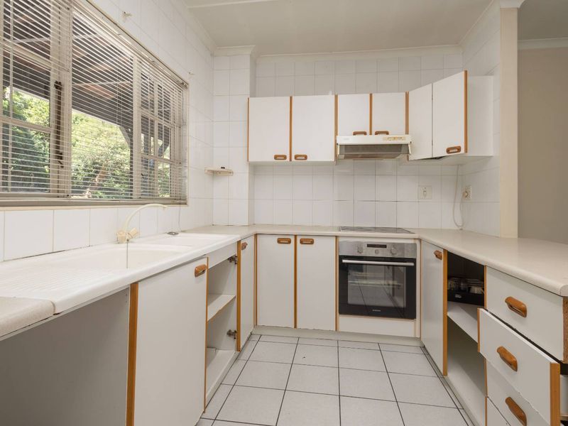 A dated kitchen featuring white cabinetry, laminate countertops, tiled backsplash, and built-in appliances, offering a blank canvas for modern renovation.