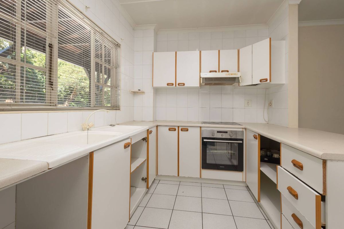 A dated kitchen featuring white cabinetry, laminate countertops, tiled backsplash, and built-in appliances, offering a blank canvas for modern renovation.