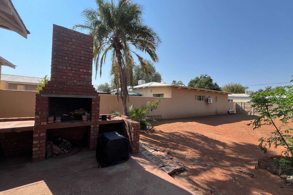 Rear garden area featuring a brick braai, concrete patio, and perimeter walling, offering a functional outdoor space with potential for landscaping improvements.