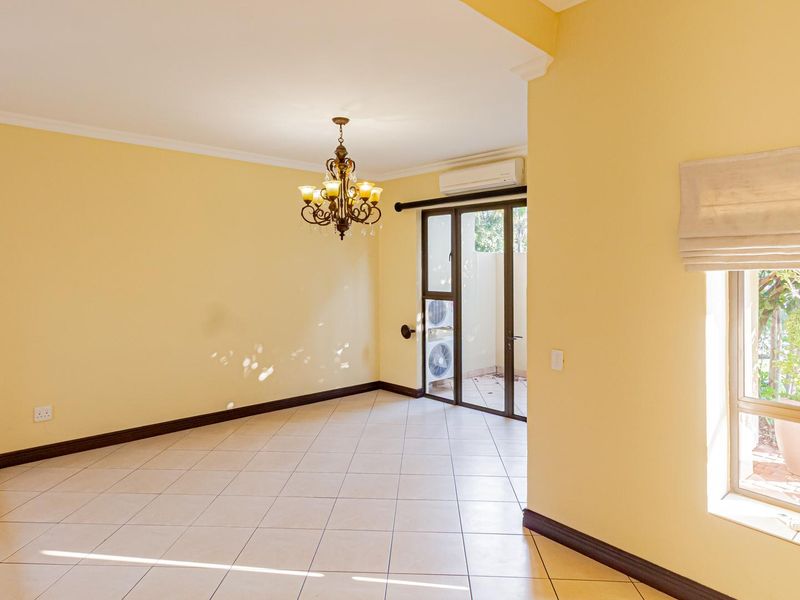 A spacious, light-filled living area featuring tiled flooring, a classic chandelier, and direct access to an outdoor patio through sliding glass doors.