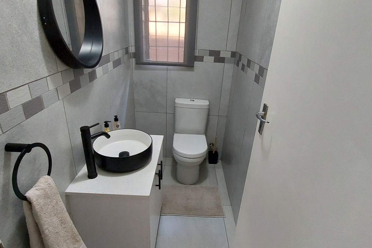 A modern guest bathroom featuring a contemporary vessel sink, vanity cabinet, and tiled walls with a decorative border.