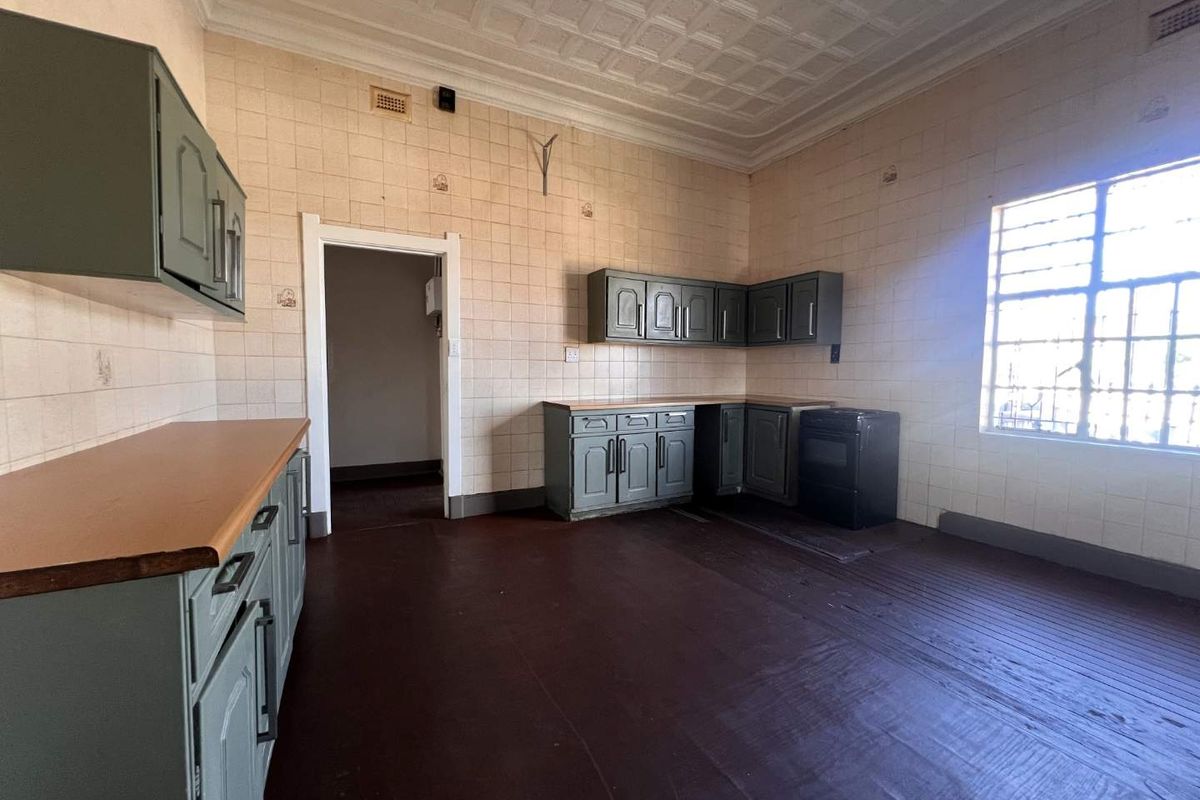 An empty, dated kitchen featuring original decorative ceiling, tiled walls, timber flooring, and built-in cabinetry with a freestanding oven.