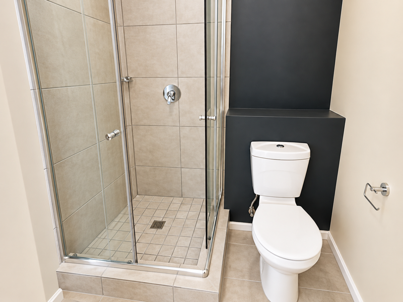 A clean, modern bathroom featuring a glass-enclosed shower with neutral tiling and a white toilet set against a contrasting dark feature wall.