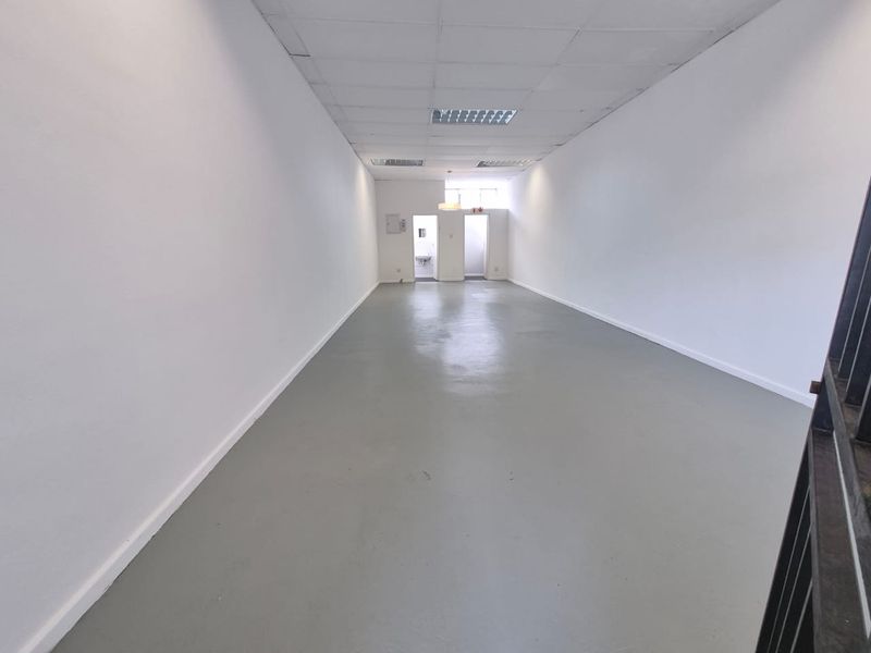 A spacious, empty open-plan retail unit featuring a neutral painted finish, suspended ceiling with recessed lighting, and a durable painted concrete floor.