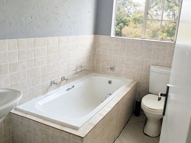 A functional bathroom featuring a built-in bathtub, toilet, and pedestal basin with tiled finishes, offering potential for modernization.