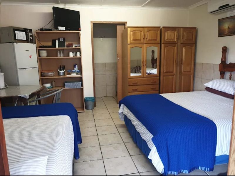 A functional bedroom featuring tiled flooring, a wall-mounted air conditioning unit, and direct access to an adjoining bathroom area.