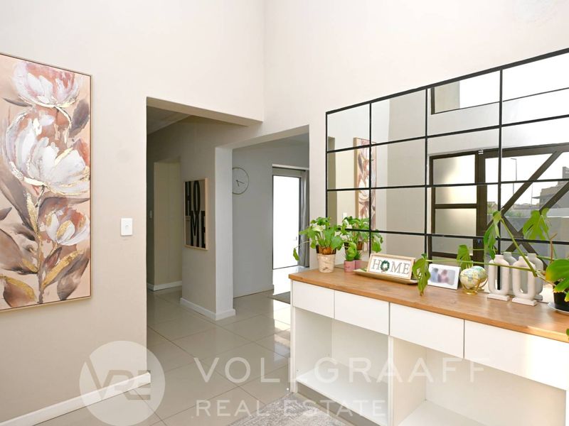 Bright and spacious entrance hall featuring high ceilings, neutral tiled flooring, and a large decorative grid-pattern wall mirror.