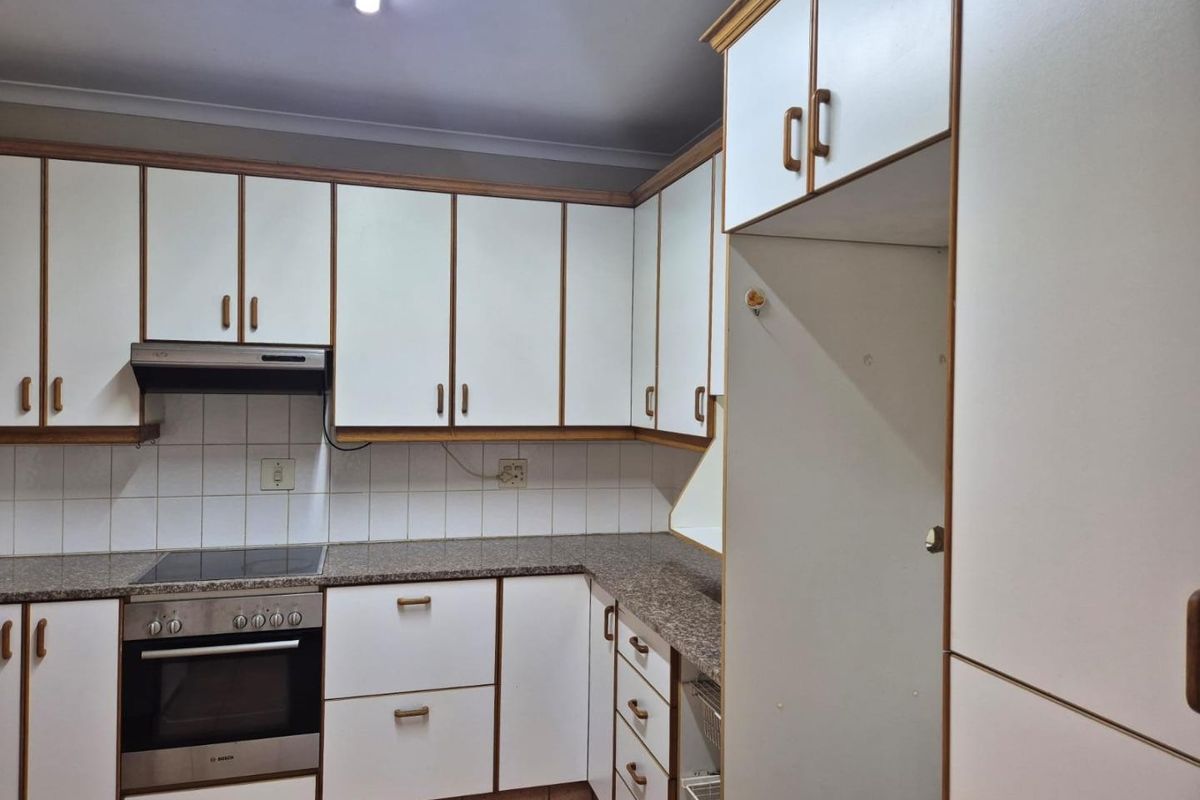 A functional kitchen featuring white cabinetry with wood trim, granite-look laminate countertops, built-in oven, electric hob, and tiled backsplash.