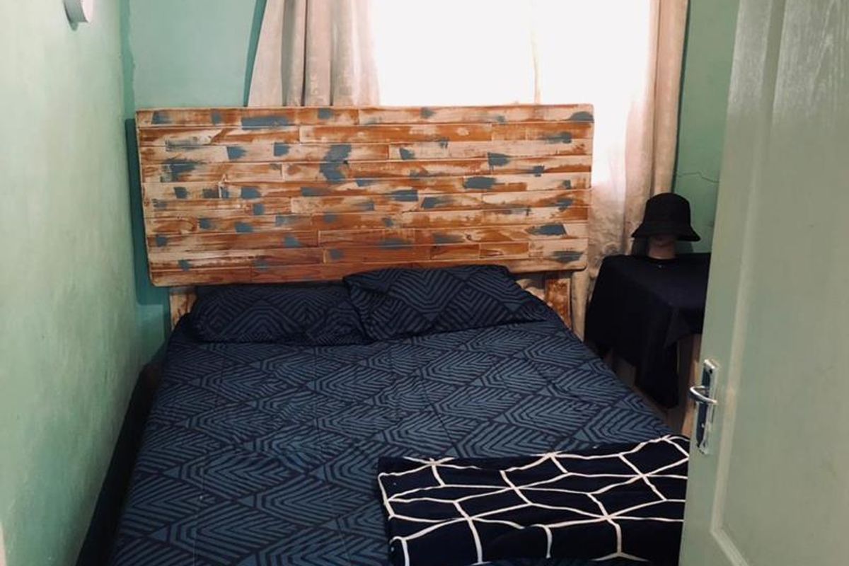 A compact bedroom featuring tiled flooring and a window with curtain rail, showing signs of wall moisture damage and wear.