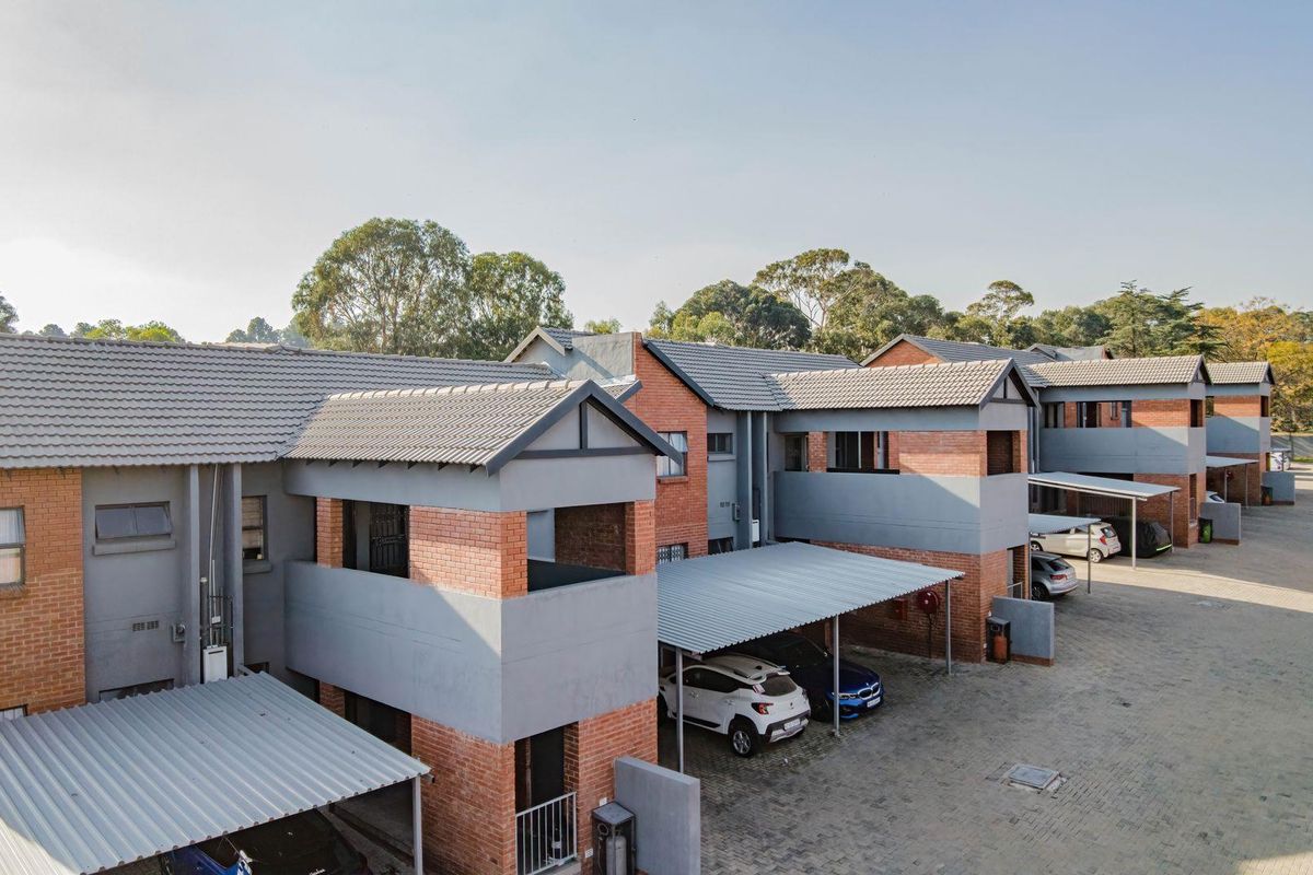 An elevated view of a multi-unit apartment complex featuring brick and rendered facades, tiled roofing, and dedicated carport parking spaces.