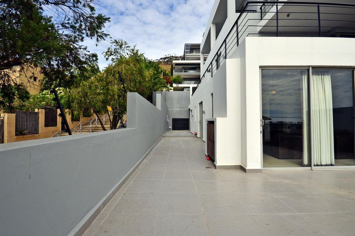 A modern exterior side walkway and patio area featuring tiled flooring, a boundary wall, and large sliding glass doors leading into the apartment.