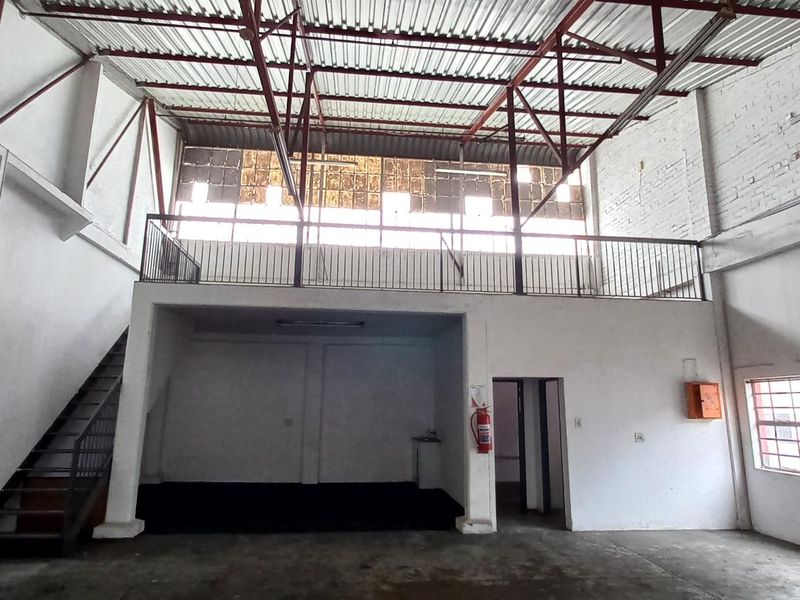 Spacious industrial unit featuring a mezzanine level, exposed steel roof trusses, and large windows, offering a versatile open-plan layout for various commercial or storage uses.