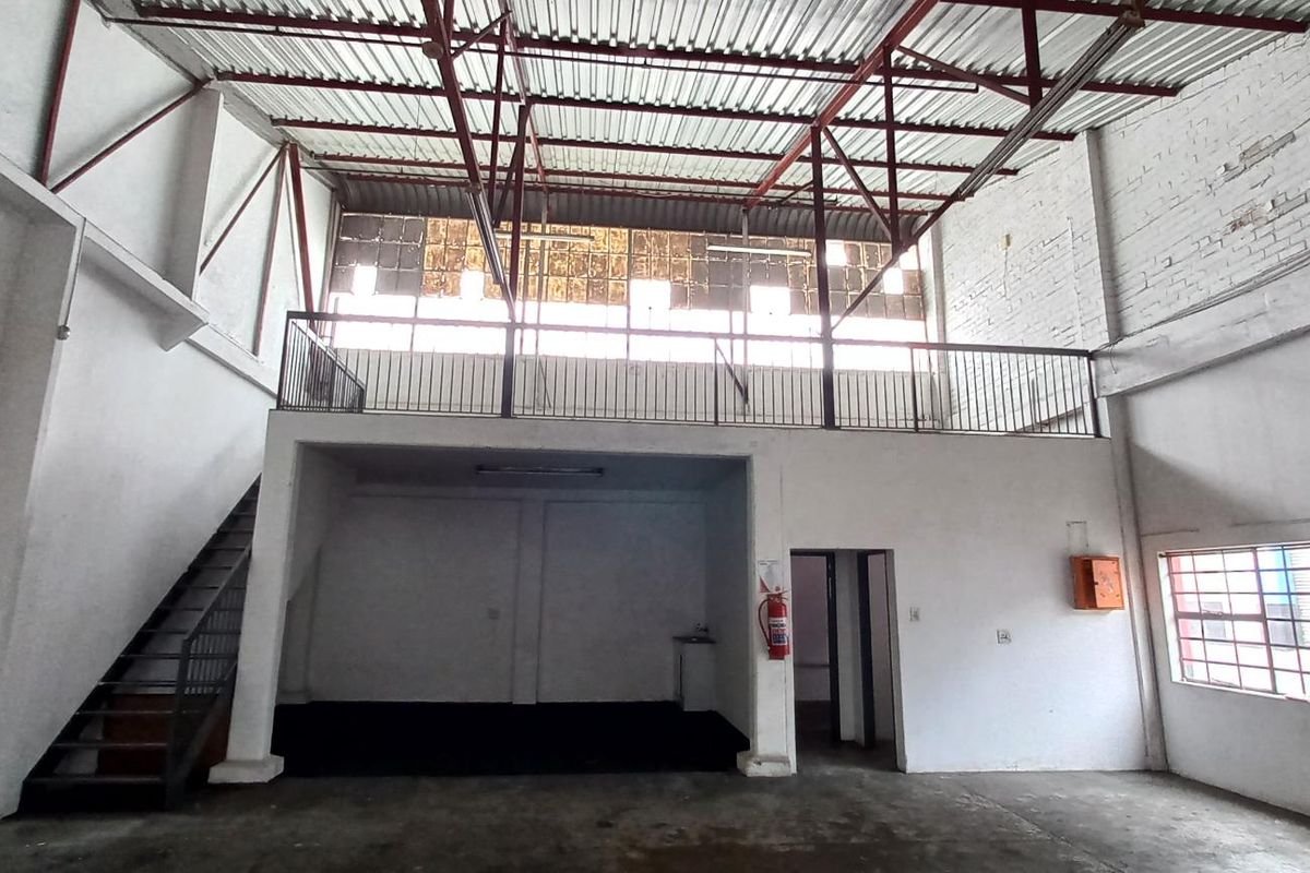 Spacious industrial unit featuring a mezzanine level, exposed steel roof trusses, and large windows, offering a versatile open-plan layout for various commercial or storage uses.
