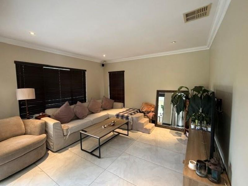 A comfortable living room featuring large format floor tiles, recessed downlighting, and dark venetian blinds, creating a neutral and functional space.