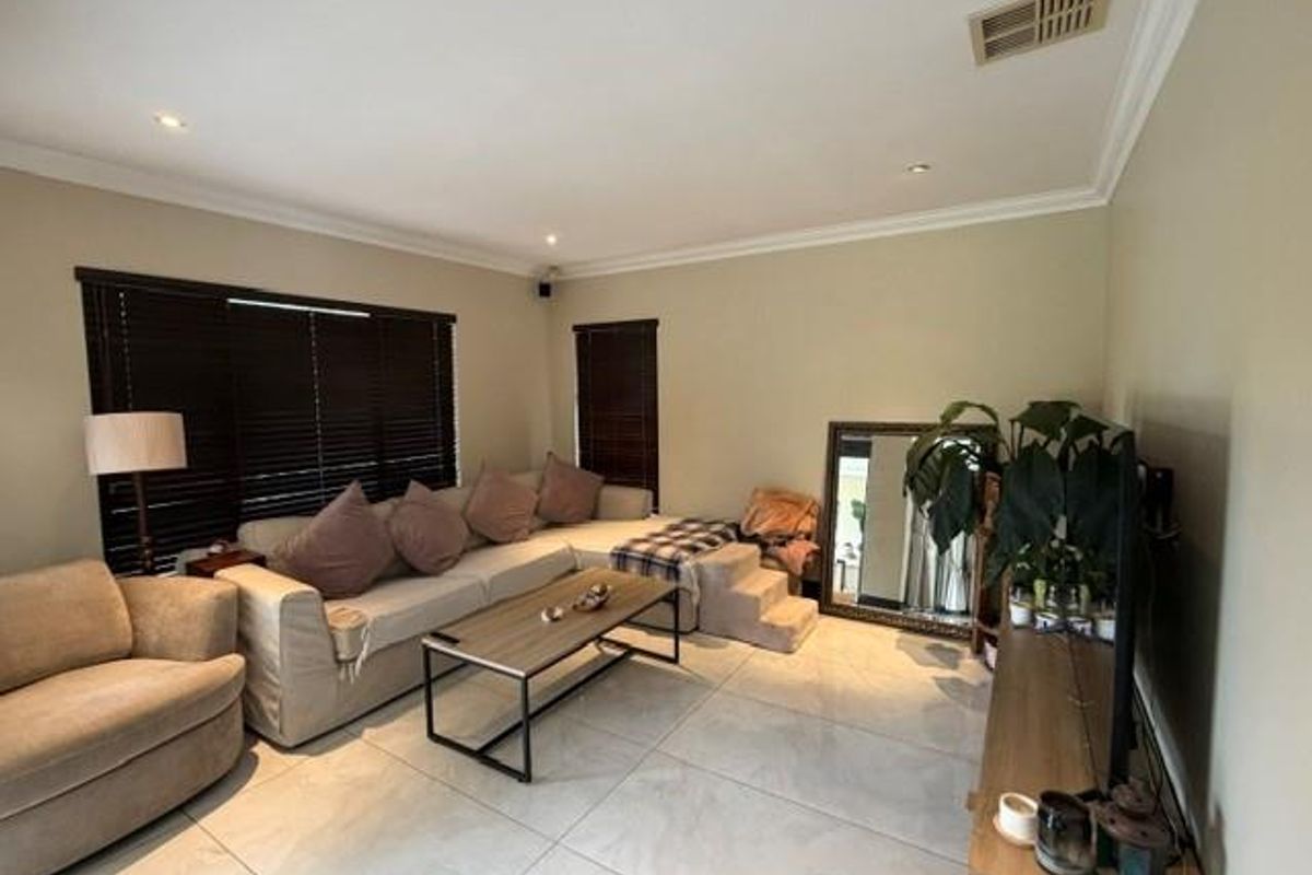 A comfortable living room featuring large format floor tiles, recessed downlighting, and dark venetian blinds, creating a neutral and functional space.