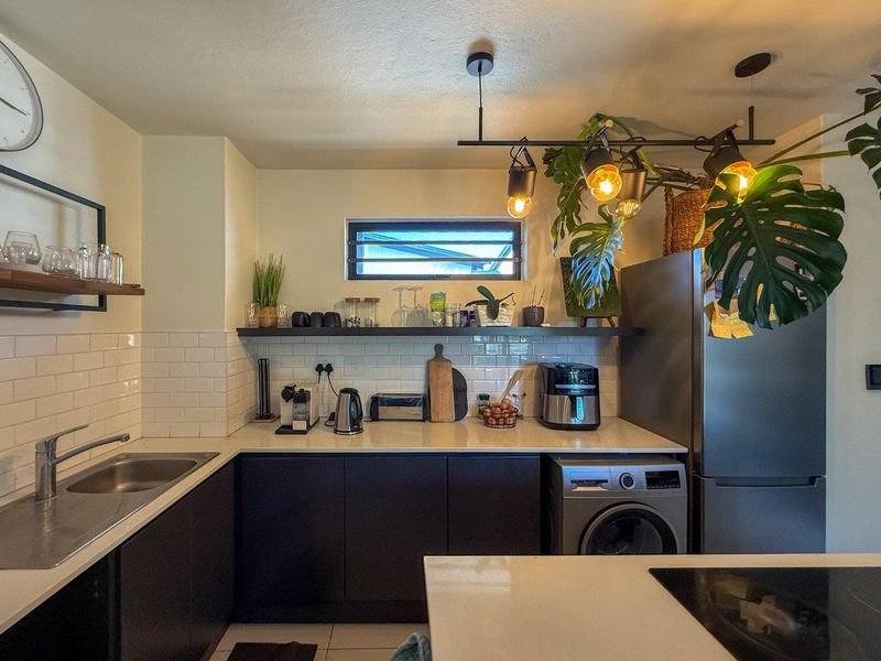 Modern kitchen featuring dark cabinetry, white subway tile backsplash, quartz countertops, and integrated laundry facilities with stylish track lighting.