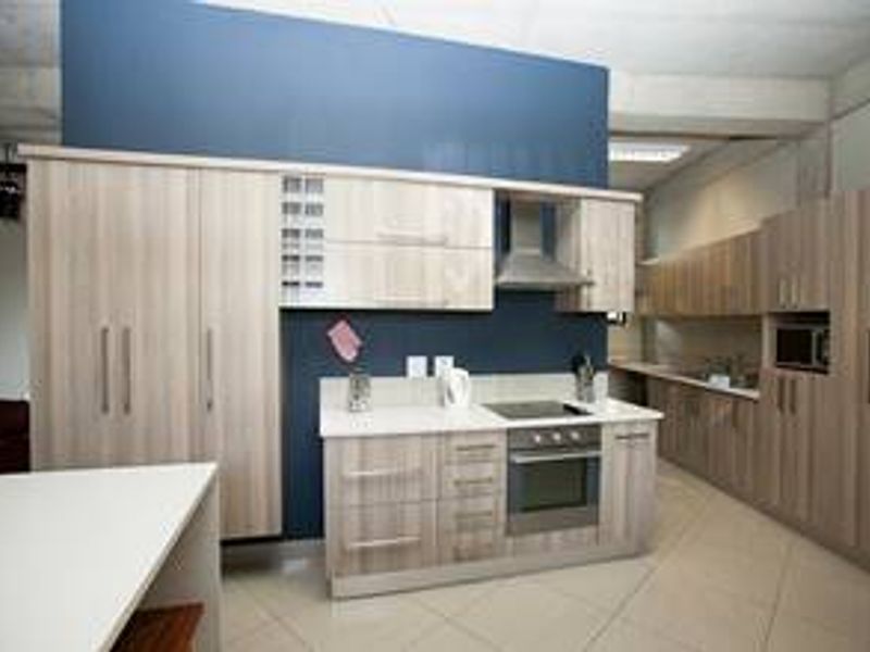 Modern kitchen featuring light wood-grain cabinetry, stone countertops, integrated appliances including an oven and hob, and a contrasting blue feature wall.