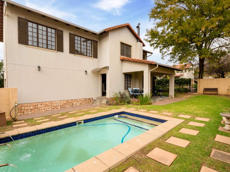 Rear view of a two-story house featuring a swimming pool, covered patio area, stone-clad base, and a landscaped garden with paved walkways.