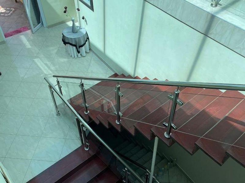 An elegant entrance hall featuring a modern staircase with dark wood treads, stainless steel balustrades, and glass panels, complemented by light-toned tiled flooring.