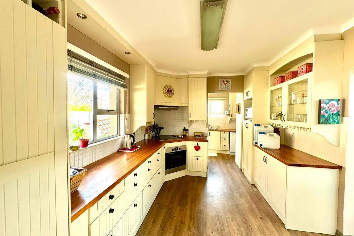 A functional kitchen featuring cream-colored cabinetry, warm wooden countertops, built-in oven, and a tiled backsplash, with a secondary prep area visible in the background.