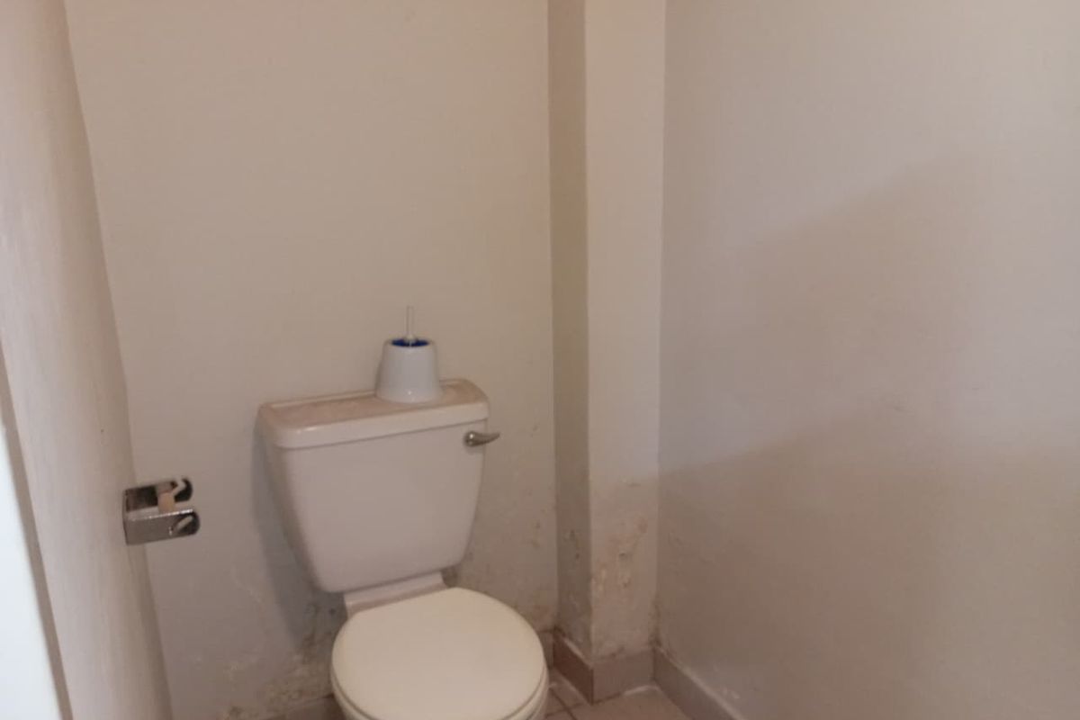A small powder room featuring a standard toilet and tiled flooring, showing signs of significant wall surface deterioration and moisture damage.