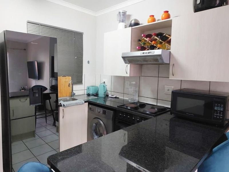 Compact kitchen featuring granite countertops, built-in cabinetry, an electric hob with extractor fan, and a tiled backsplash.