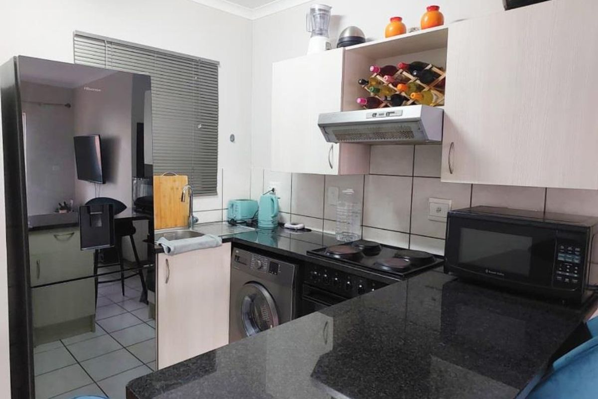 Compact kitchen featuring granite countertops, built-in cabinetry, an electric hob with extractor fan, and a tiled backsplash.