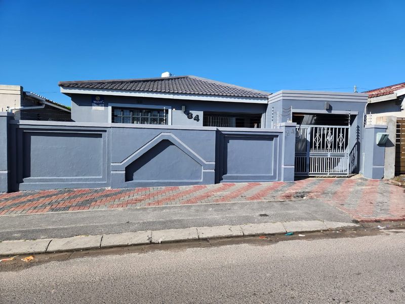 Front elevation of a residential property featuring a secure perimeter wall, gated driveway access, and a tiled roof structure.