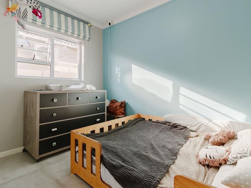 A well-maintained bedroom featuring neutral tiled flooring, a large sliding window, and a blue accent wall.