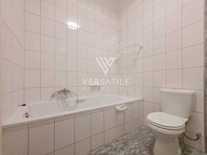 A functional bathroom featuring full-height wall tiling, a standard bathtub with shower mixer, and a white toilet.