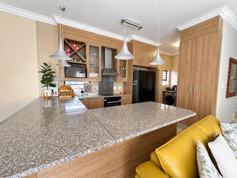 Modern open-plan kitchen featuring granite countertops, wood-finish cabinetry, built-in appliances, and stylish pendant lighting, seamlessly integrated with the living area.