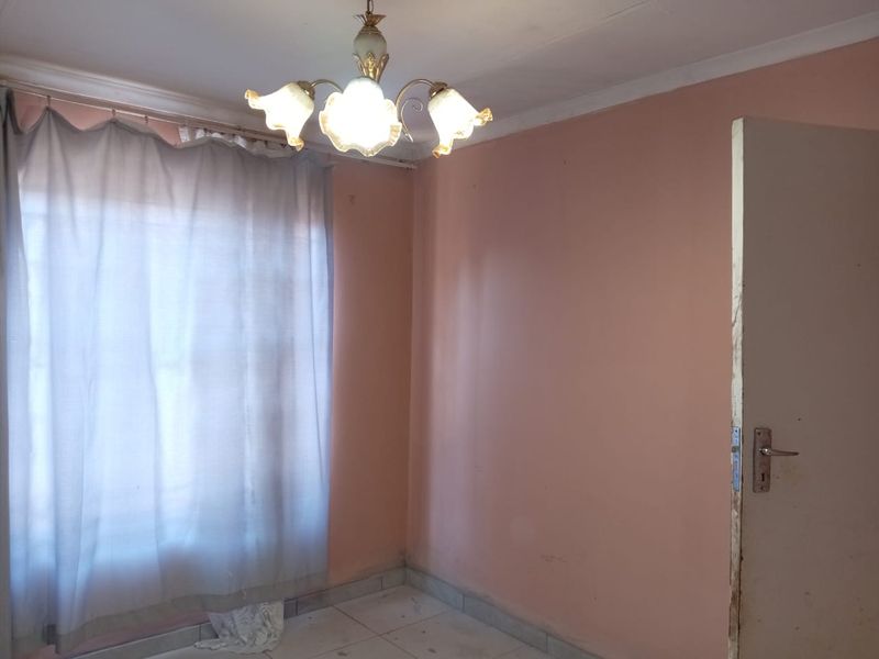 An empty bedroom featuring tiled flooring, a central light fixture, and a standard internal door, requiring cosmetic updates to improve its overall condition.