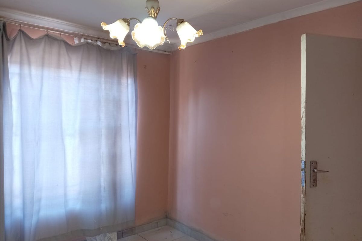 An empty bedroom featuring tiled flooring, a central light fixture, and a standard internal door, requiring cosmetic updates to improve its overall condition.