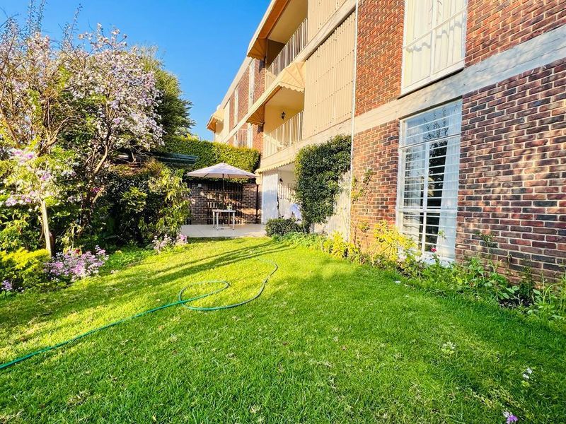 Rear view of the apartment building featuring a private garden, lawn area, and a paved patio space accessible from the ground floor.