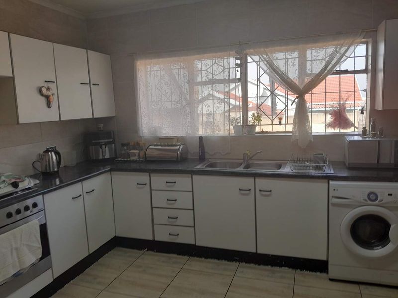 A functional kitchen featuring white built-in cabinetry, laminate countertops, a double bowl sink, and tiled flooring with integrated oven and laundry appliance space.