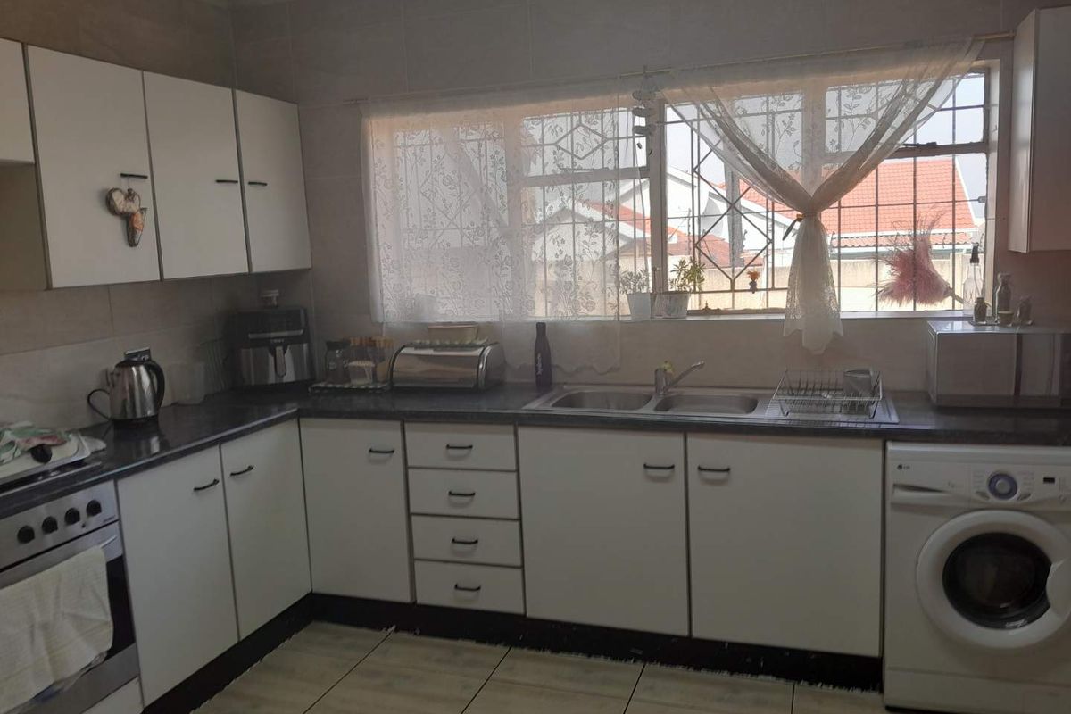 A functional kitchen featuring white built-in cabinetry, laminate countertops, a double bowl sink, and tiled flooring with integrated oven and laundry appliance space.
