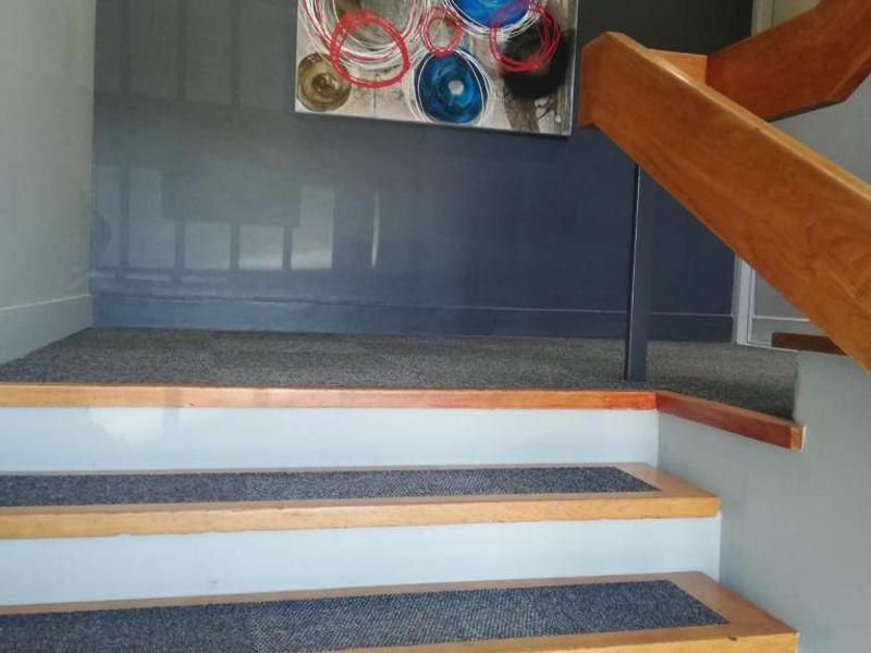 A well-maintained office staircase featuring wooden steps with carpeted treads and a sturdy wooden handrail, illuminated by recessed ceiling lights.