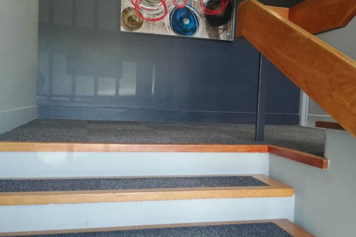 A well-maintained office staircase featuring wooden steps with carpeted treads and a sturdy wooden handrail, illuminated by recessed ceiling lights.