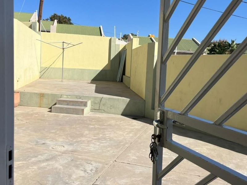 A private rear courtyard featuring concrete paving, a raised patio area, and secure metal gate access, requiring some maintenance and cosmetic updates.
