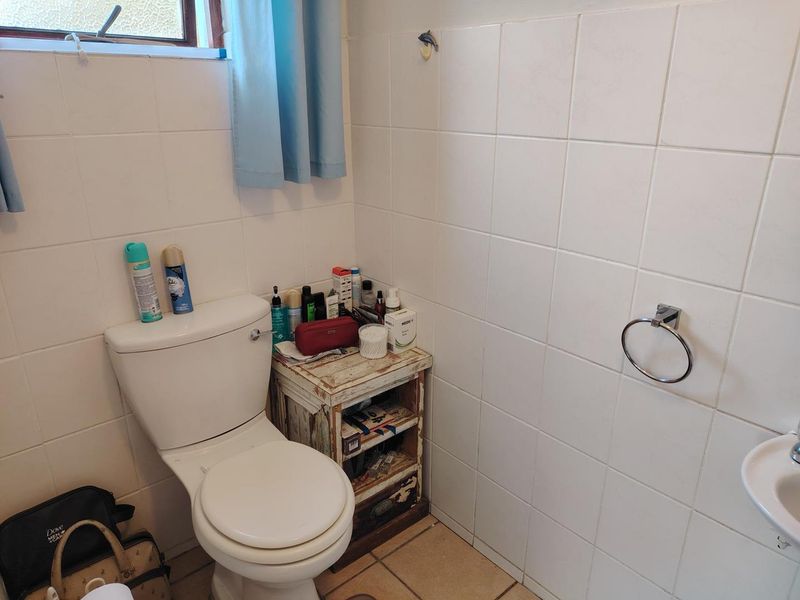 A compact bathroom featuring white wall tiles, a standard toilet, and a wall-mounted wash basin with a towel ring.