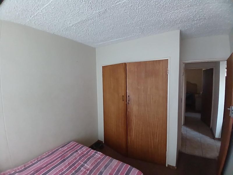 A bedroom featuring a built-in wooden wardrobe and textured ceiling, requiring cosmetic updates to improve the overall aesthetic.
