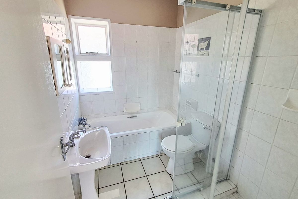 A functional bathroom featuring a pedestal basin, bathtub, and a separate shower enclosure with tiled finishes throughout.