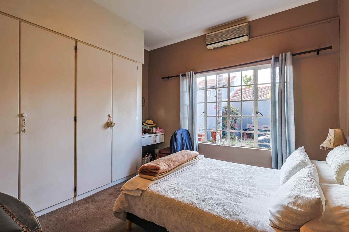 A bedroom featuring built-in cupboards, a wall-mounted air conditioning unit, and a window overlooking the rear garden area.