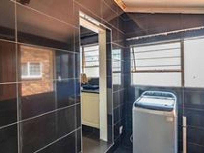 A laundry area featuring dark wall tiles, security bars on the window, and direct access to the kitchen.