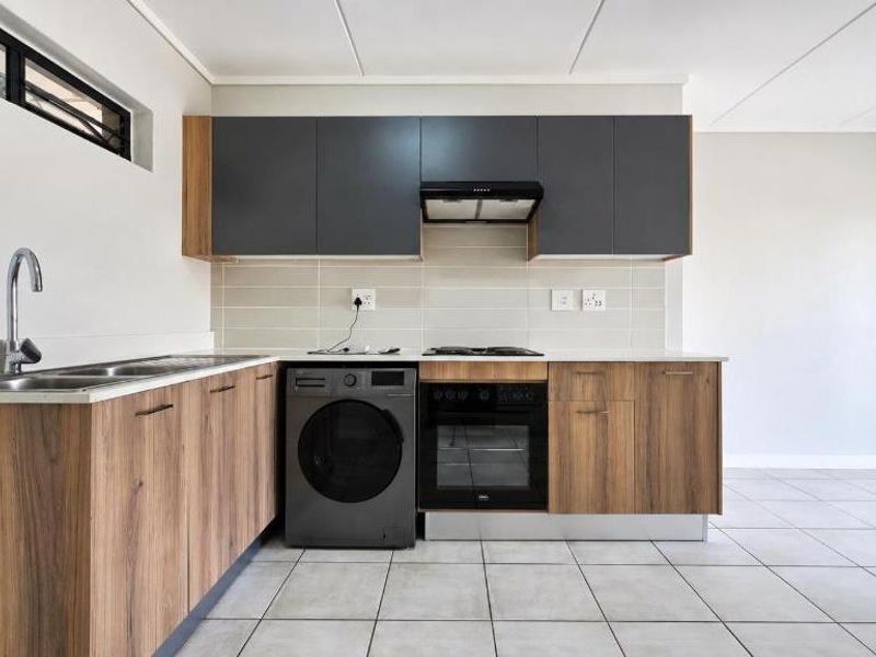 Modern kitchen featuring wood-grain cabinetry, dark grey upper cabinets, built-in oven, hob, extractor fan, and neutral tiled flooring.