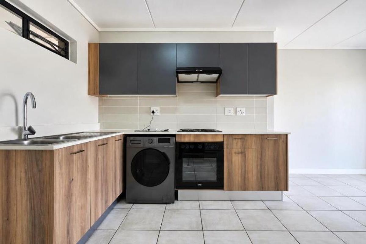 Modern kitchen featuring wood-grain cabinetry, dark grey upper cabinets, built-in oven, hob, extractor fan, and neutral tiled flooring.