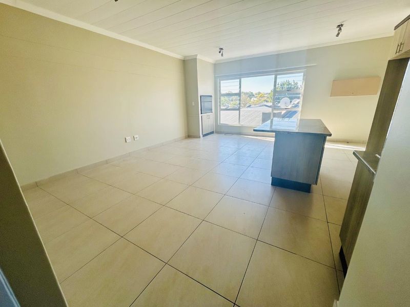 Spacious open-plan living and kitchen area featuring neutral tiled flooring, a central kitchen island, and large windows providing ample natural light.