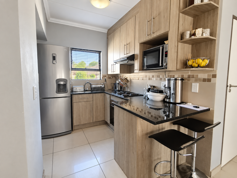 Modern kitchen featuring light wood-grain cabinetry, dark granite countertops, a breakfast bar, and integrated appliances including an oven, hob, and microwave.