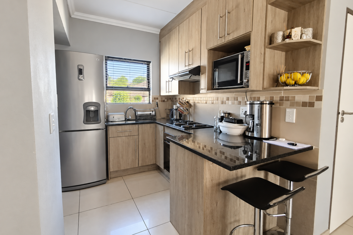Modern kitchen featuring light wood-grain cabinetry, dark granite countertops, a breakfast bar, and integrated appliances including an oven, hob, and microwave.