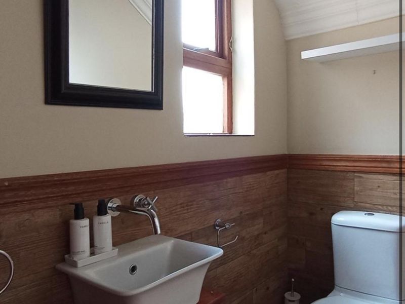 A compact bathroom featuring timber-look wall panelling, a wall-mounted basin with chrome fixtures, and a modern dual-flush toilet.